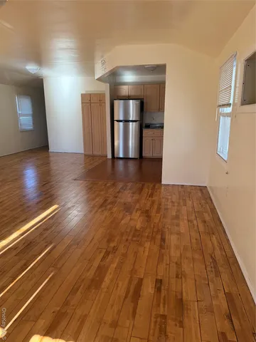 a view of empty room with wooden floor and kitchen