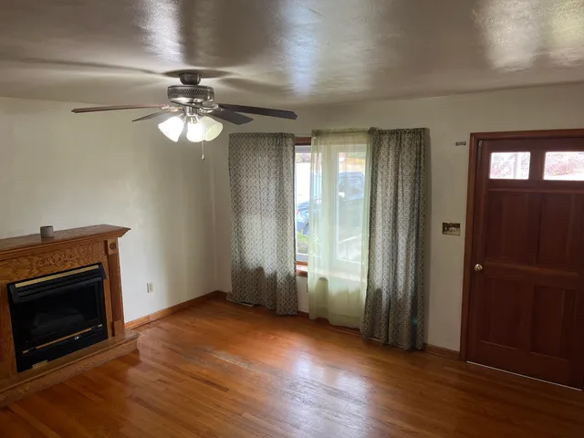 an empty room with wooden floor a ceiling fan a fireplace and windows