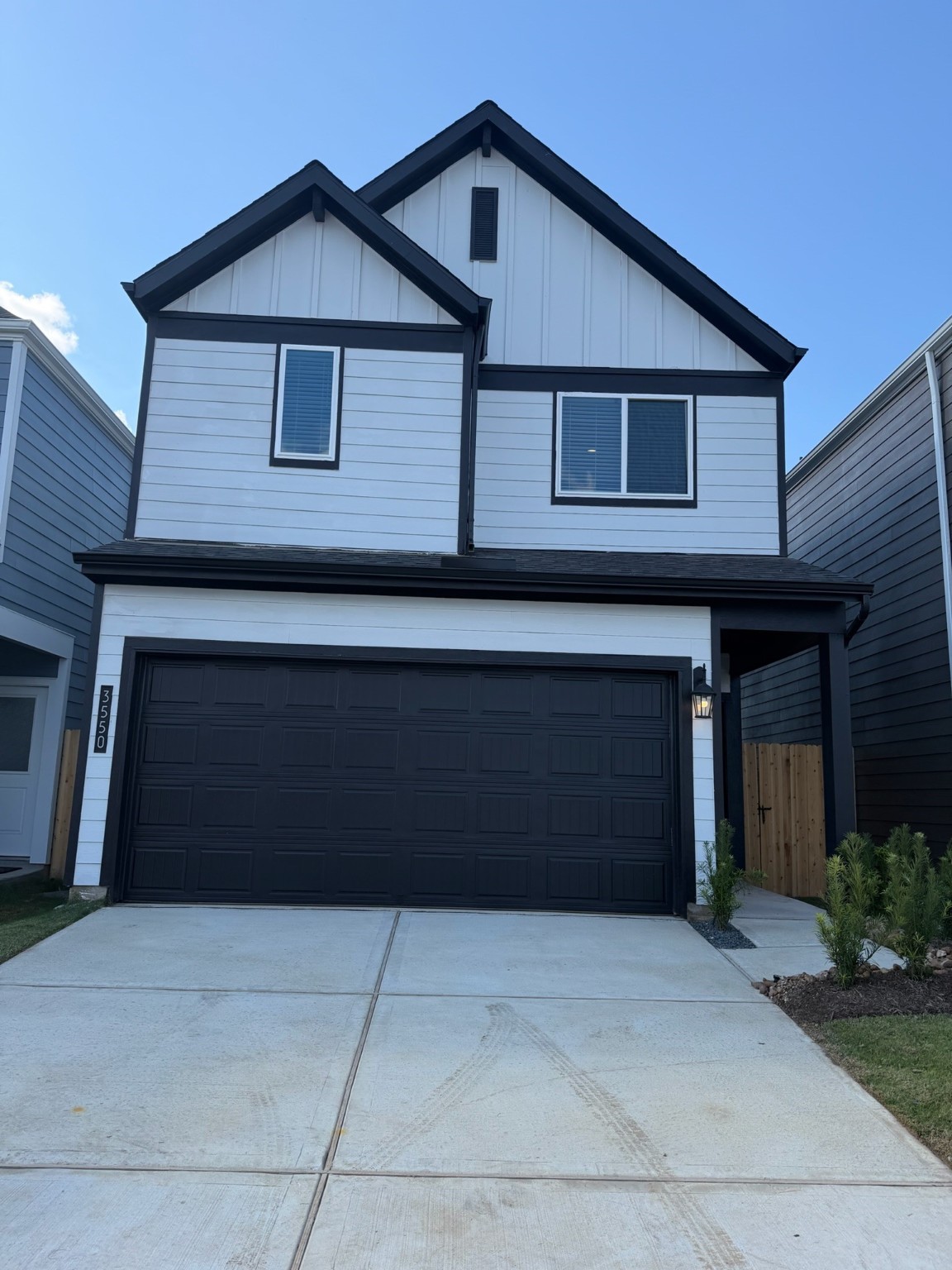 Modern two-story home with a sleek black and white exterior, featuring a spacious garage and a simple driveway.