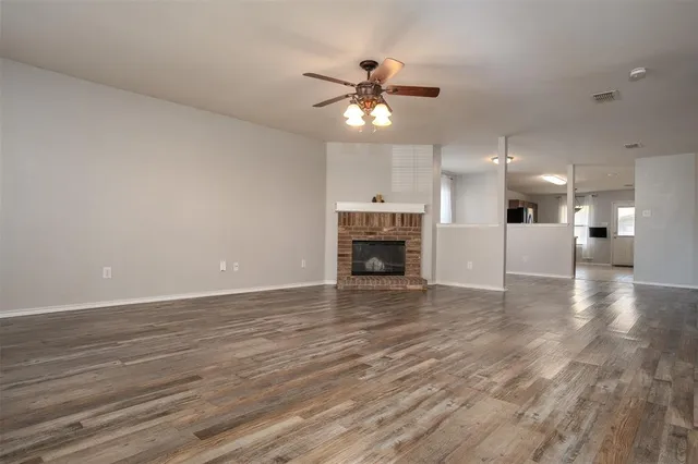 a view of a livingroom with a fireplace a ceiling fan and wooden floor
