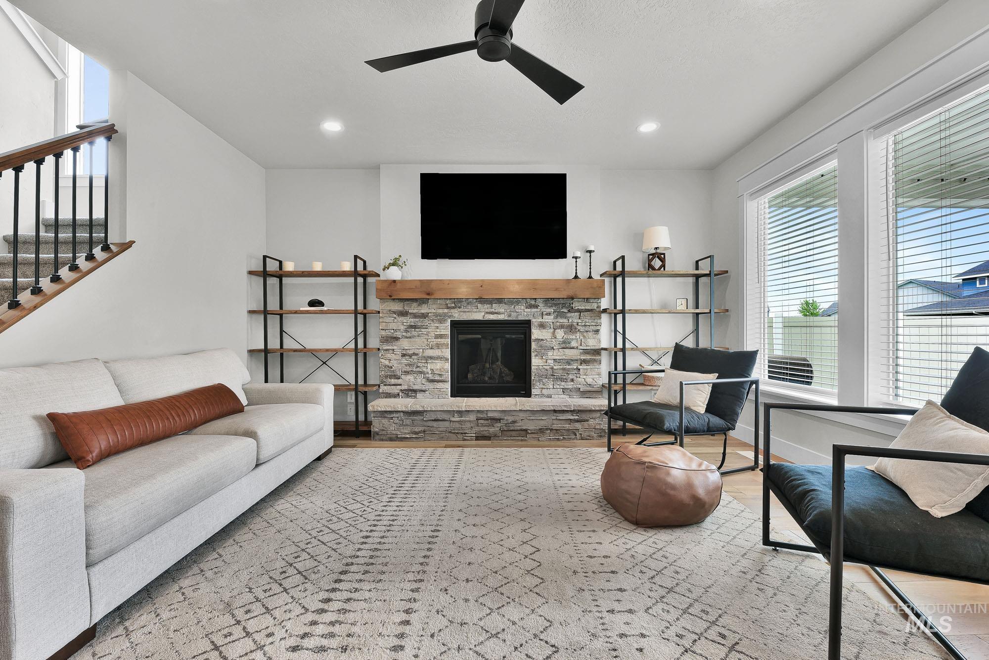 5676 East Zaffre Ridge Street Boise, ID 83716 - Photo 21 of 50 Living area featuring a stone-clad fireplace with a wood mantel, wood-finish flooring, a contemporary ceiling fan, and large windows with blinds