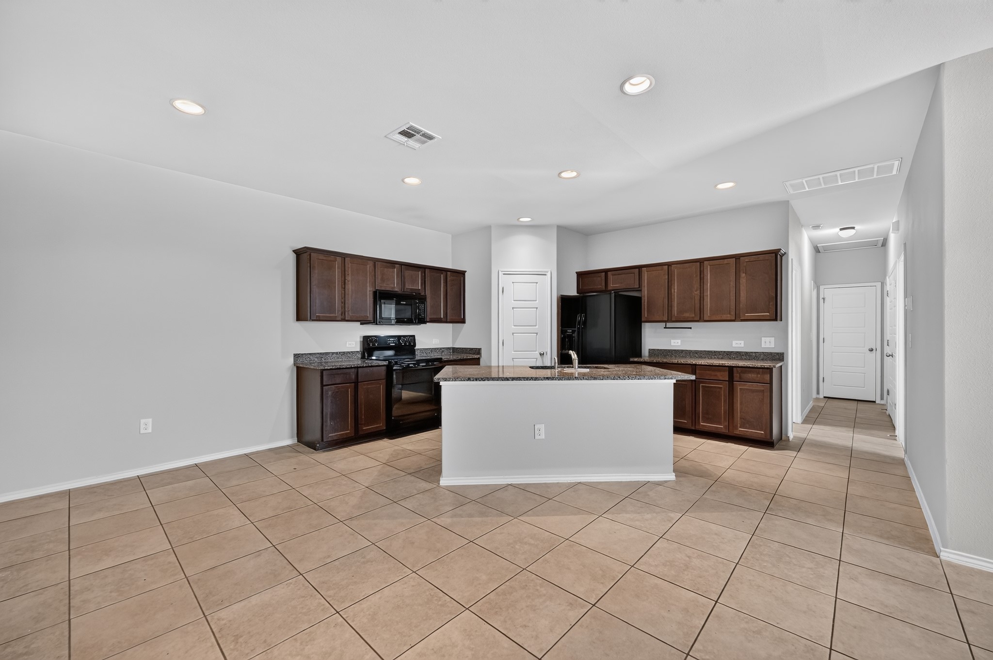 Durable tile flooring spans this open kitchen containing rich wood cabinetry and a central island.