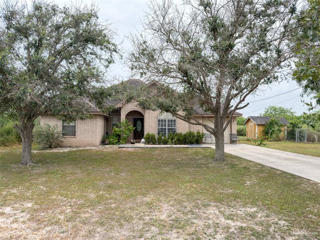 7435 Dillon Road Donna, TX 78537 - Photo 13 of 17 Brick exterior home with an arched entry, mature front yard trees, a paved driveway, and a detached storage shed