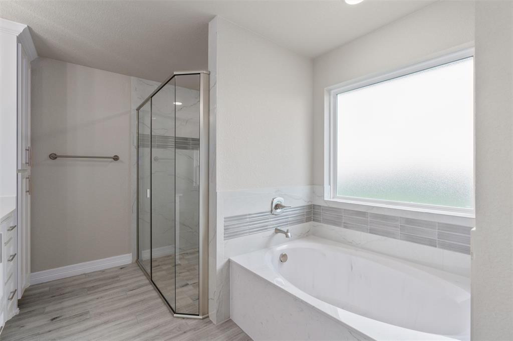 1341 Promised Land Road Hewitt, TX 76643 - Photo 18 of 29 Soaking tub with a tiled surround, frosted window, glass-enclosed shower, wood-finish flooring, and white cabinetry