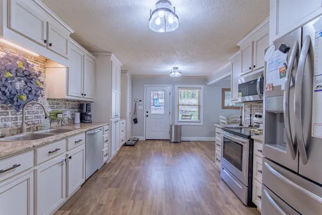 a kitchen with stainless steel appliances granite countertop a refrigerator a stove a sink and white cabinets with wooden floor