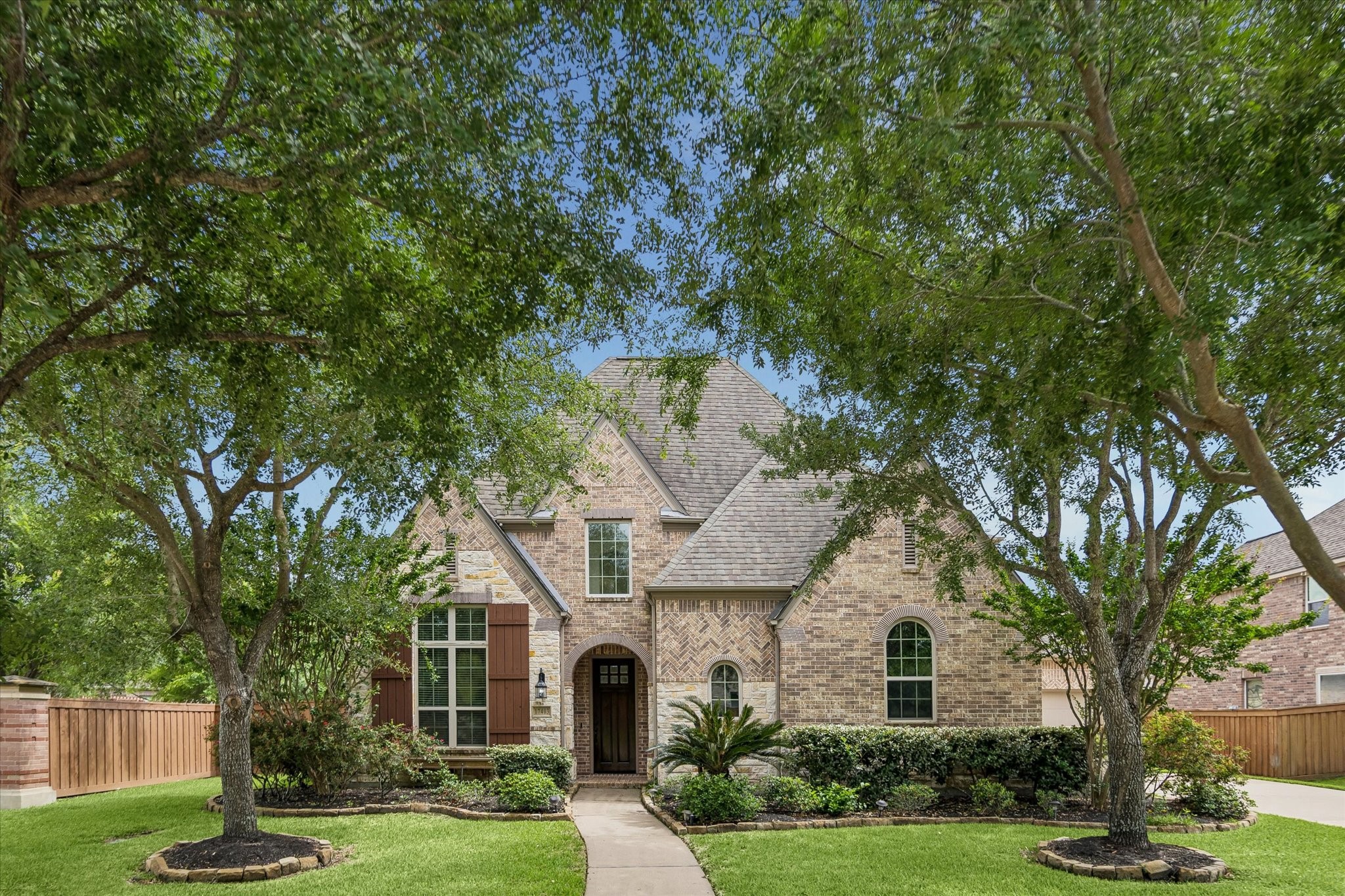 17403 Astrachan Road Richmond, TX 77407 - Photo 1 of 40 This charming home features a classic brick facade with arched windows. It is set in a lush, landscaped yard with mature trees providing shade and a welcoming walkway leading to the entrance.