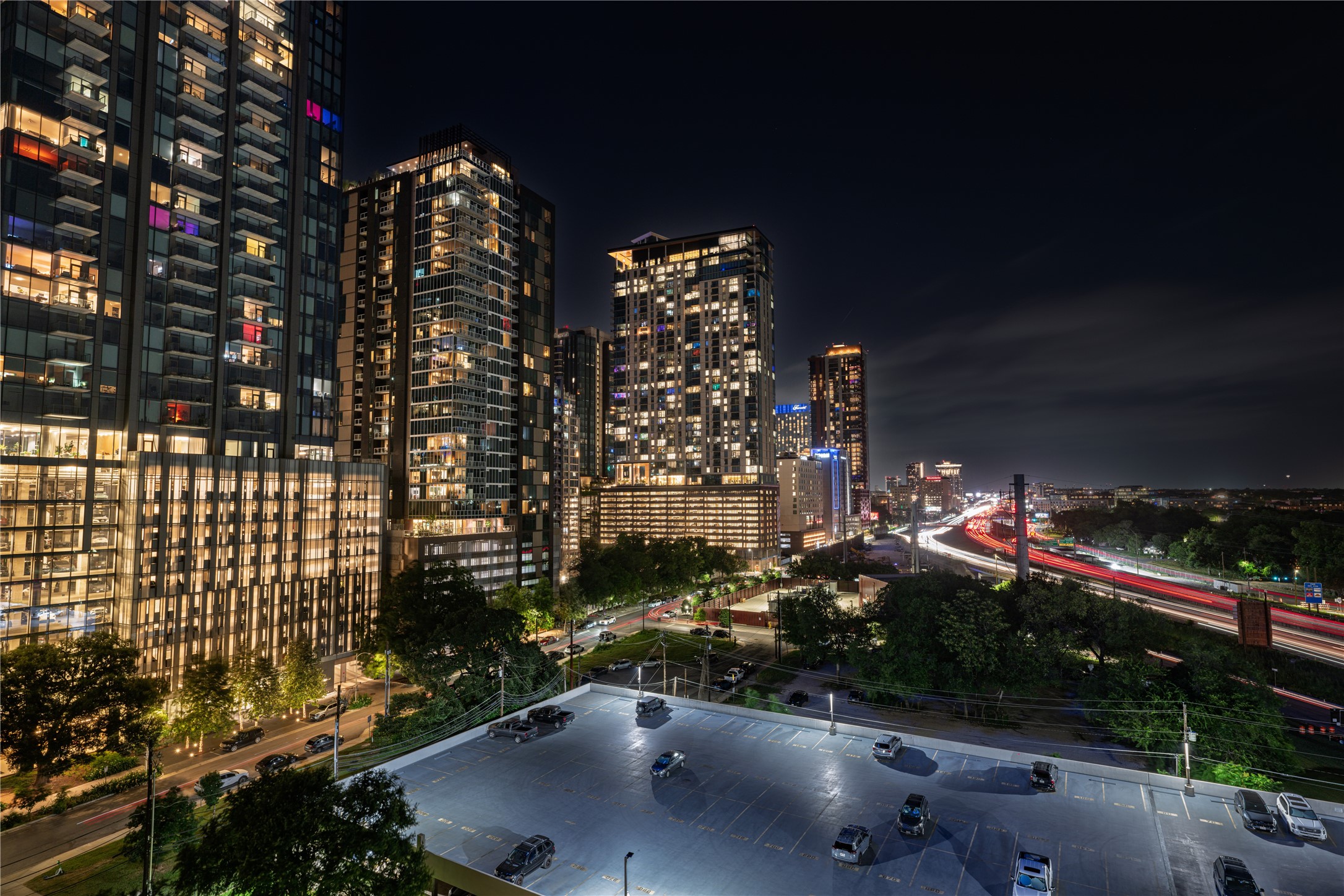40 North Interstate Highway 35, Unit 11B2 Austin, TX 78701 - Photo 4 of 28 A vibrant cityscape lights up the night, with sleek high-rises framing a bustling highway and an illuminated parking area.