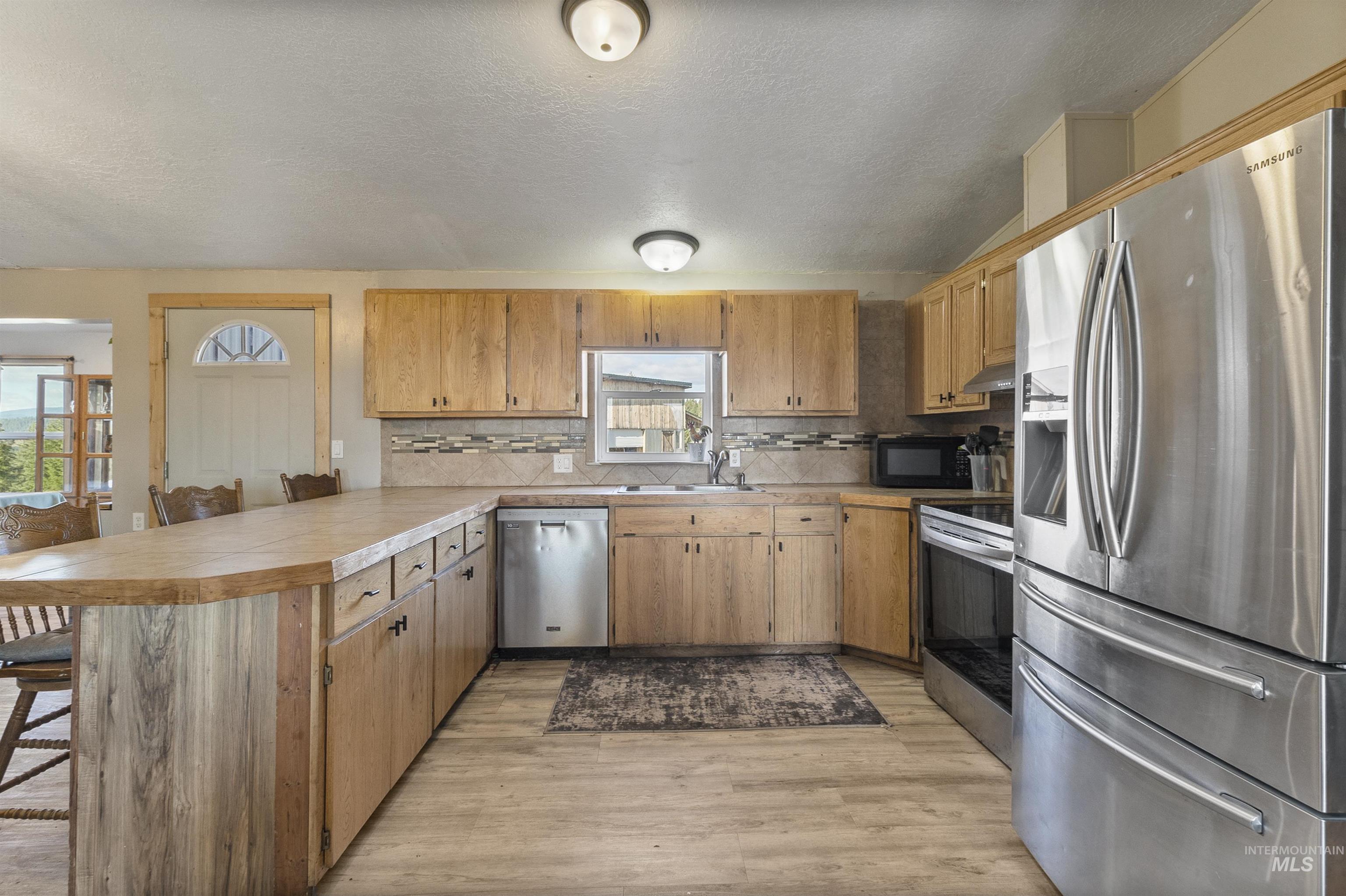 1311 Gold Hill Road Princeton, ID 83857 - Photo 11 of 25 Kitchen with stainless steel appliances, a breakfast bar, a peninsula, a textured ceiling, and backsplash