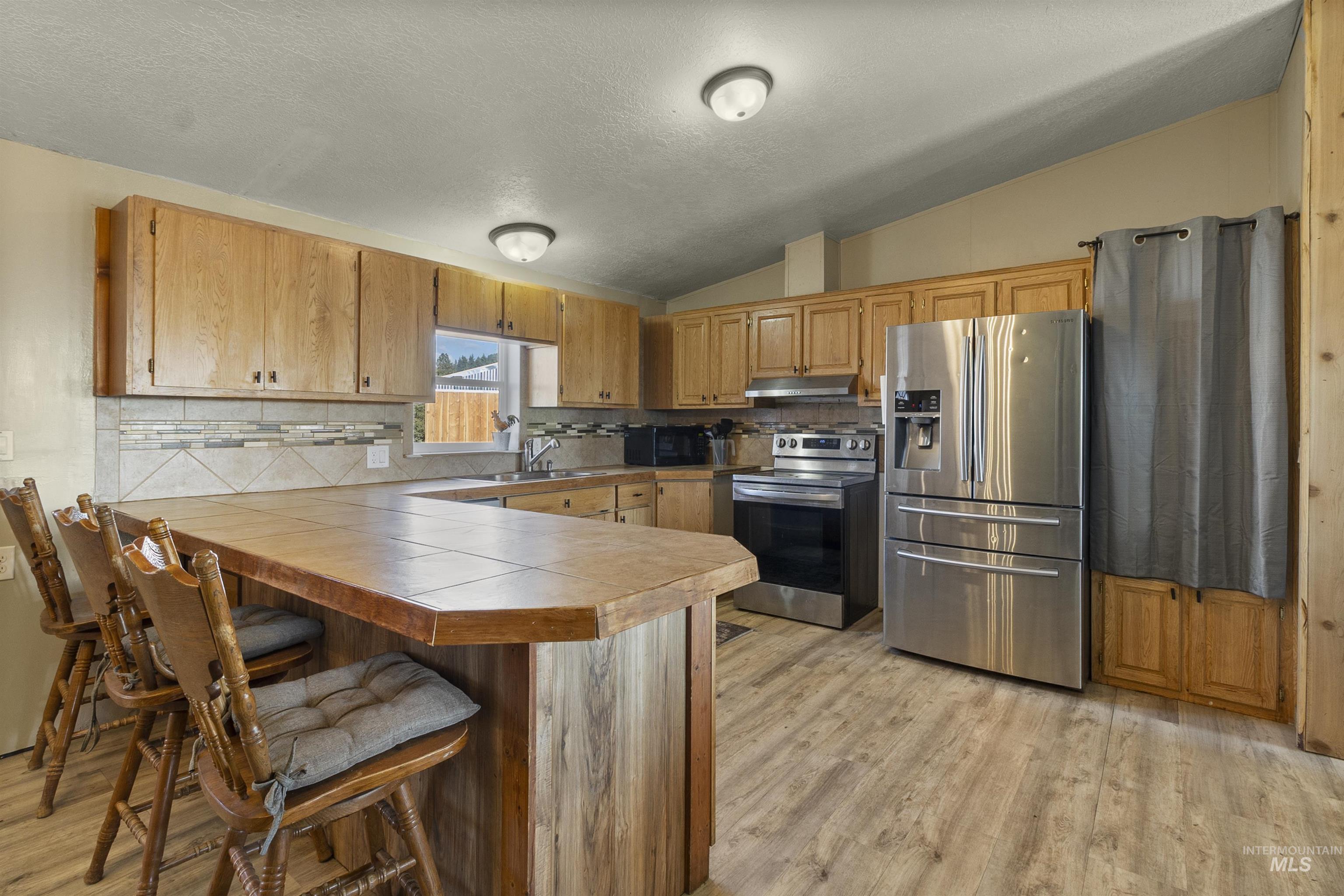 1311 Gold Hill Road Princeton, ID 83857 - Photo 12 of 25 Kitchen featuring lofted ceiling, a kitchen breakfast bar, stainless steel appliances, a textured ceiling, and light wood finished floors
