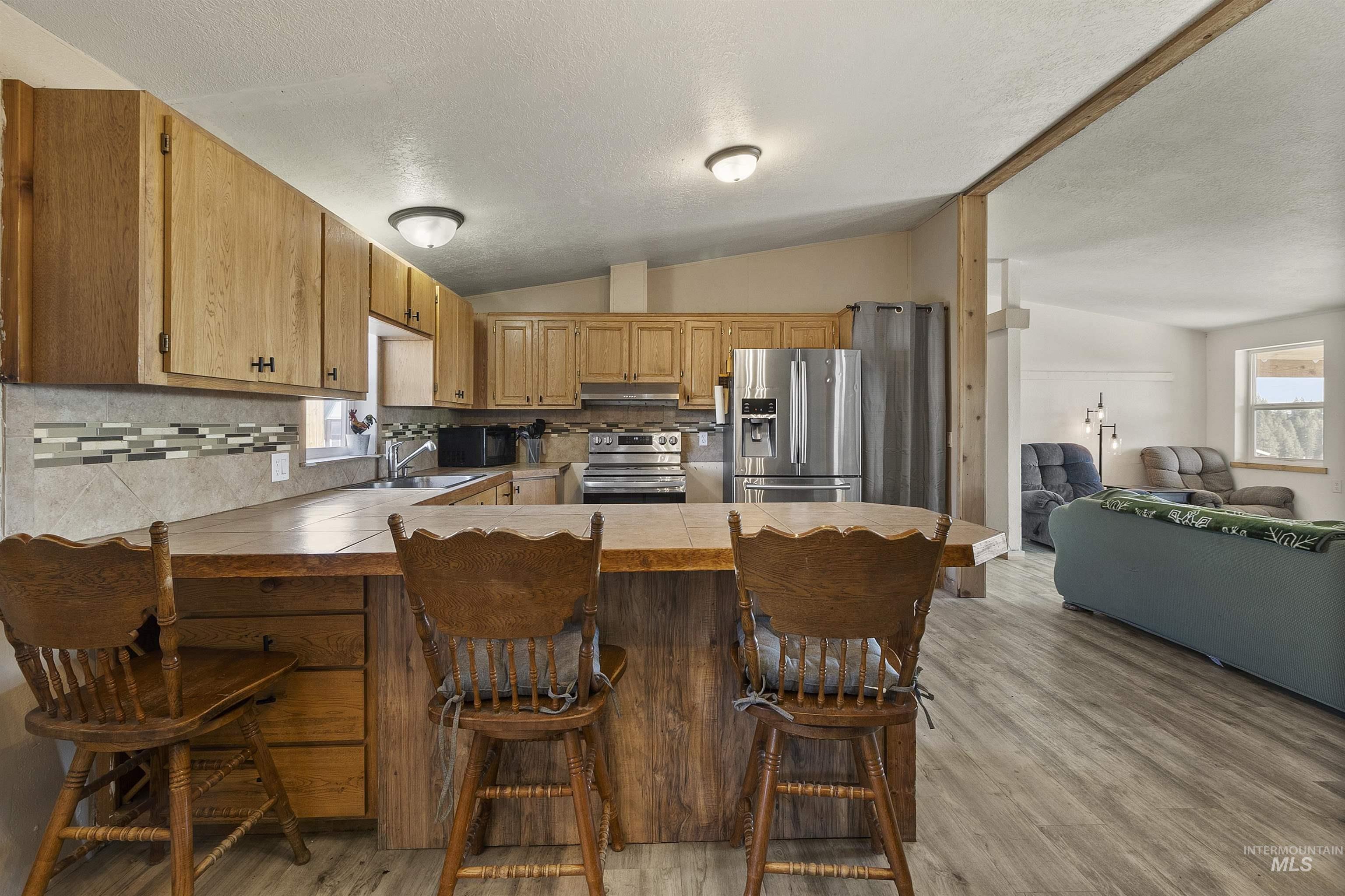1311 Gold Hill Road Princeton, ID 83857 - Photo 13 of 25 Kitchen featuring backsplash, appliances with stainless steel finishes, a breakfast bar area, a textured ceiling, and light wood-style flooring