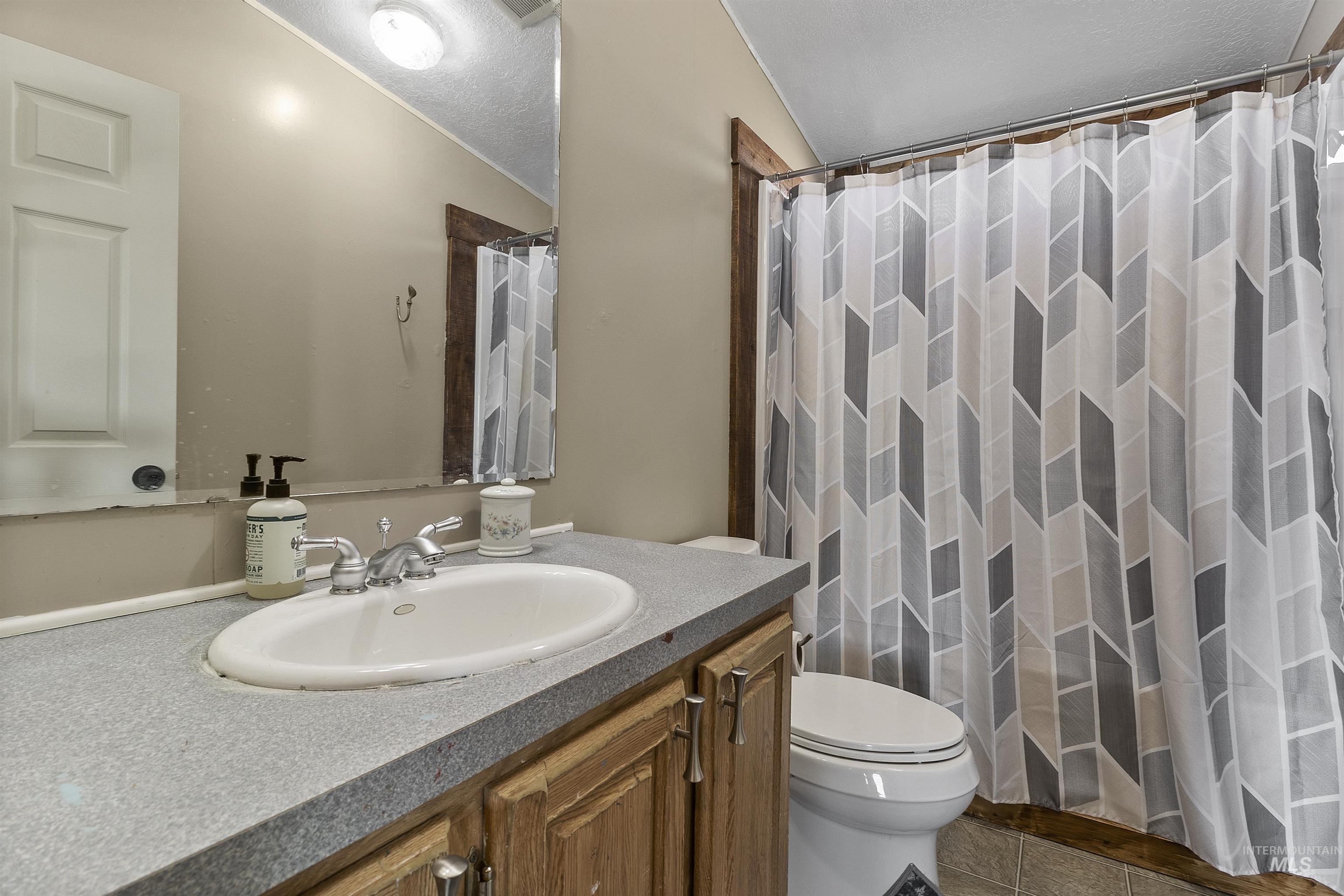 1311 Gold Hill Road Princeton, ID 83857 - Photo 7 of 25 Bathroom featuring a shower with shower curtain, vanity, dark tile patterned flooring, a textured ceiling, and vaulted ceiling