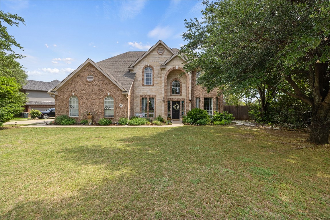 Traditional-style home featuring a front lawn, fence, stone siding, brick siding, and a shingled roof