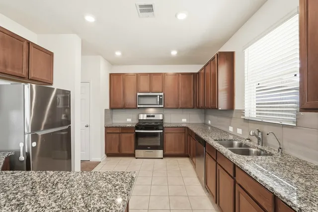 a large kitchen with stainless steel appliances granite countertop a sink stove refrigerator and cabinets