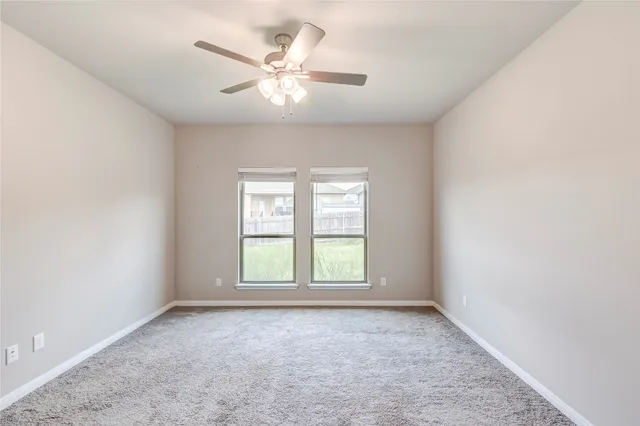 an empty room with a chandelier fan and windows