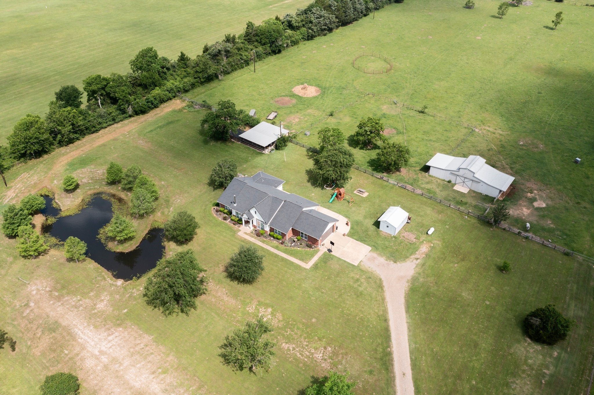 34334 Howell Road Waller, TX 77484 - Photo 6 of 37 This aerial perspective reveals the unique layout of this property, featuring a charming home, a tranquil pond, and various outbuildings, all nestled within a vast expanse of land. Enjoy the peaceful setting and the endless possibilities this property offers.