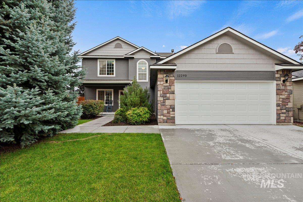 View of front of house with stone siding, driveway, a front yard, and an attached garage