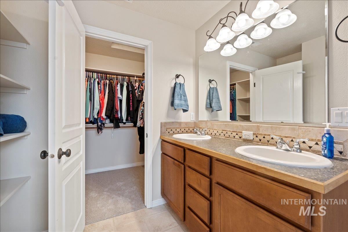 12293 West Murchison Street Boise, ID 83709 - Photo 17 of 27 Bathroom featuring a spacious closet, double vanity, decorative backsplash, and a chandelier