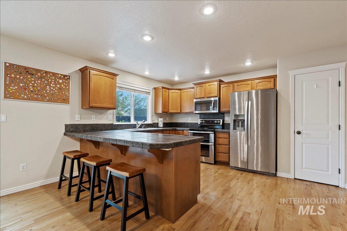12293 West Murchison Street Boise, ID 83709 - Photo 8 of 27 Kitchen with appliances with stainless steel finishes, a kitchen breakfast bar, recessed lighting, light wood-style floors, and a peninsula