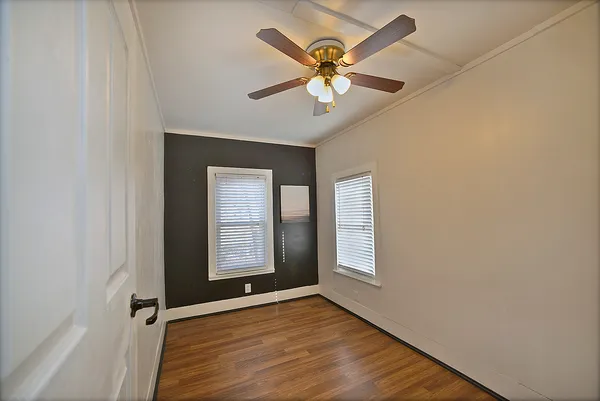 an empty room with wooden floor chandelier fan and windows