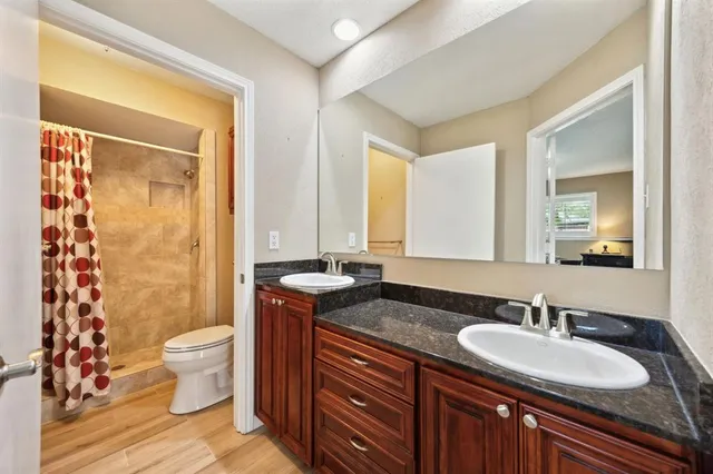 a bathroom with a granite countertop sink a toilet a mirror a vanity and shower