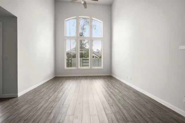 an empty room with wooden floor fan and windows