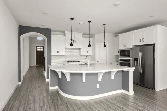 a large kitchen with stainless steel appliances granite countertop a stove a refrigerator a sink a microwave and wooden floor