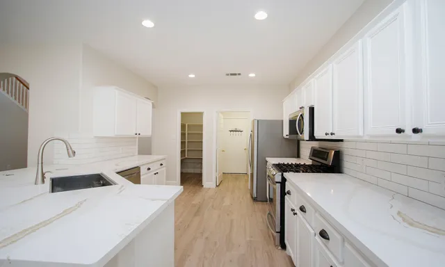 a kitchen with stainless steel appliances a stove top oven a sink a refrigerator and white cabinets