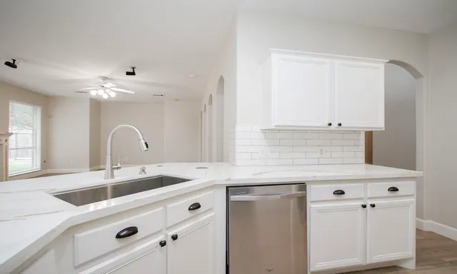 a kitchen with stainless steel appliances granite countertop a sink and white cabinets with wooden floor