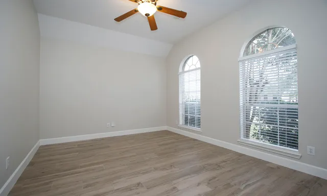 an empty room with wooden floor chandelier fan and windows