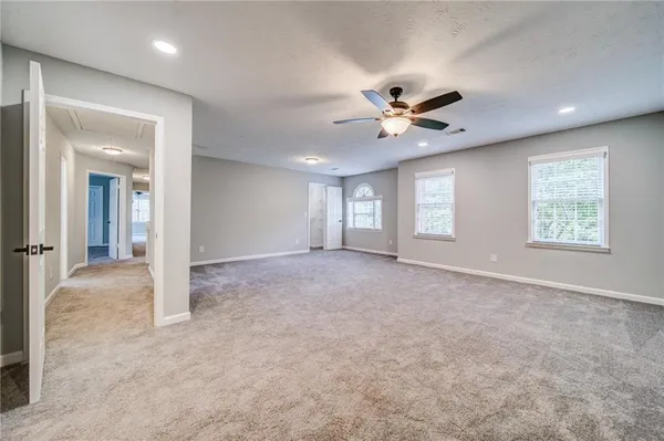 an empty room with chandelier fan and windows