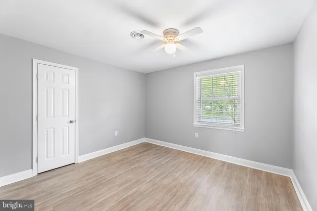 an empty room with wooden floor chandelier fan and windows