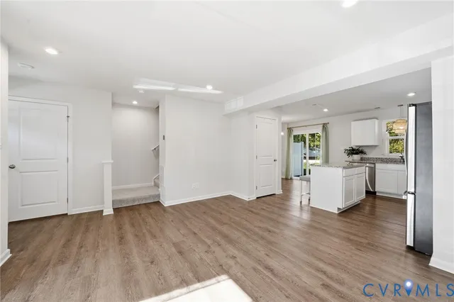 a view of an empty room and kitchen with hardwood floor