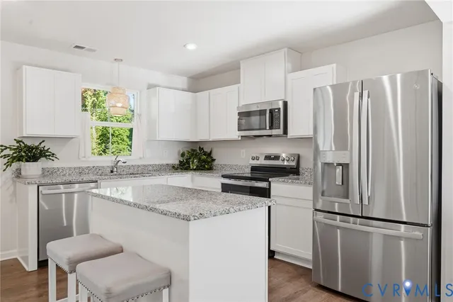 a kitchen with stainless steel appliances granite countertop a refrigerator a stove a sink a microwave a dining table and chairs with wooden floor