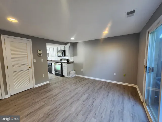 an empty room with wooden floor kitchen view and a appliances