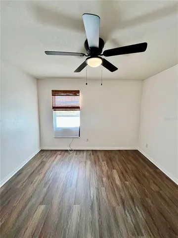 an empty room with wooden floor chandelier fan and windows