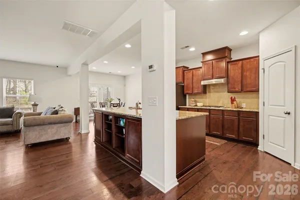 a kitchen with stainless steel appliances kitchen island granite countertop a stove top oven a sink a refrigerator white cabinets and couches