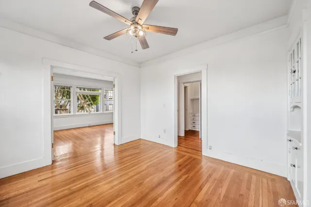 an empty room with wooden floor chandelier fan and windows