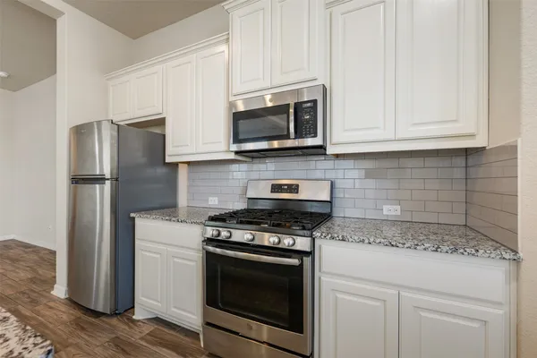 a kitchen with stainless steel appliances granite countertop white cabinets and a stove a refrigerator with wooden floor