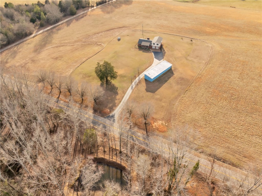 An aerial perspective reveals a charming home nestled amidst expansive fields and a tranquil pond.