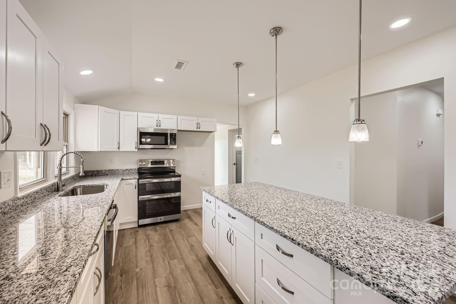 3225 Liberty Road Gold Hill, NC 28071 - Photo 7 of 24 a large kitchen with kitchen island a stove a sink a refrigerator and white cabinets with wooden floor