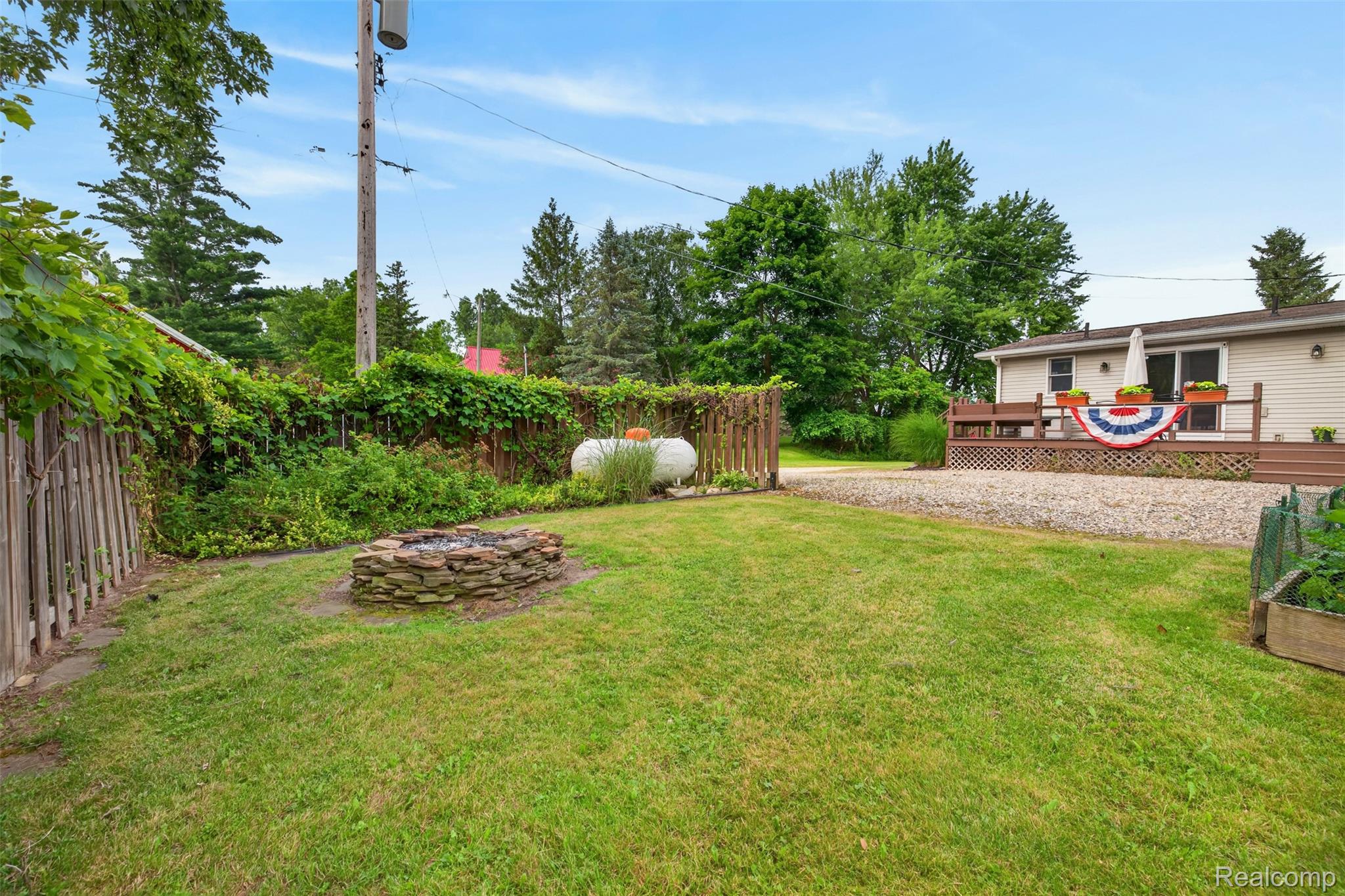 5977 Anglers Road Ortonville, MI 48462 - Photo 55 of 63 Expansive green lawn featuring a stone fire pit, wood fencing, and mature trees