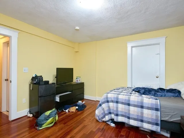 a bedroom with a bed a desk and chair with wooden floor