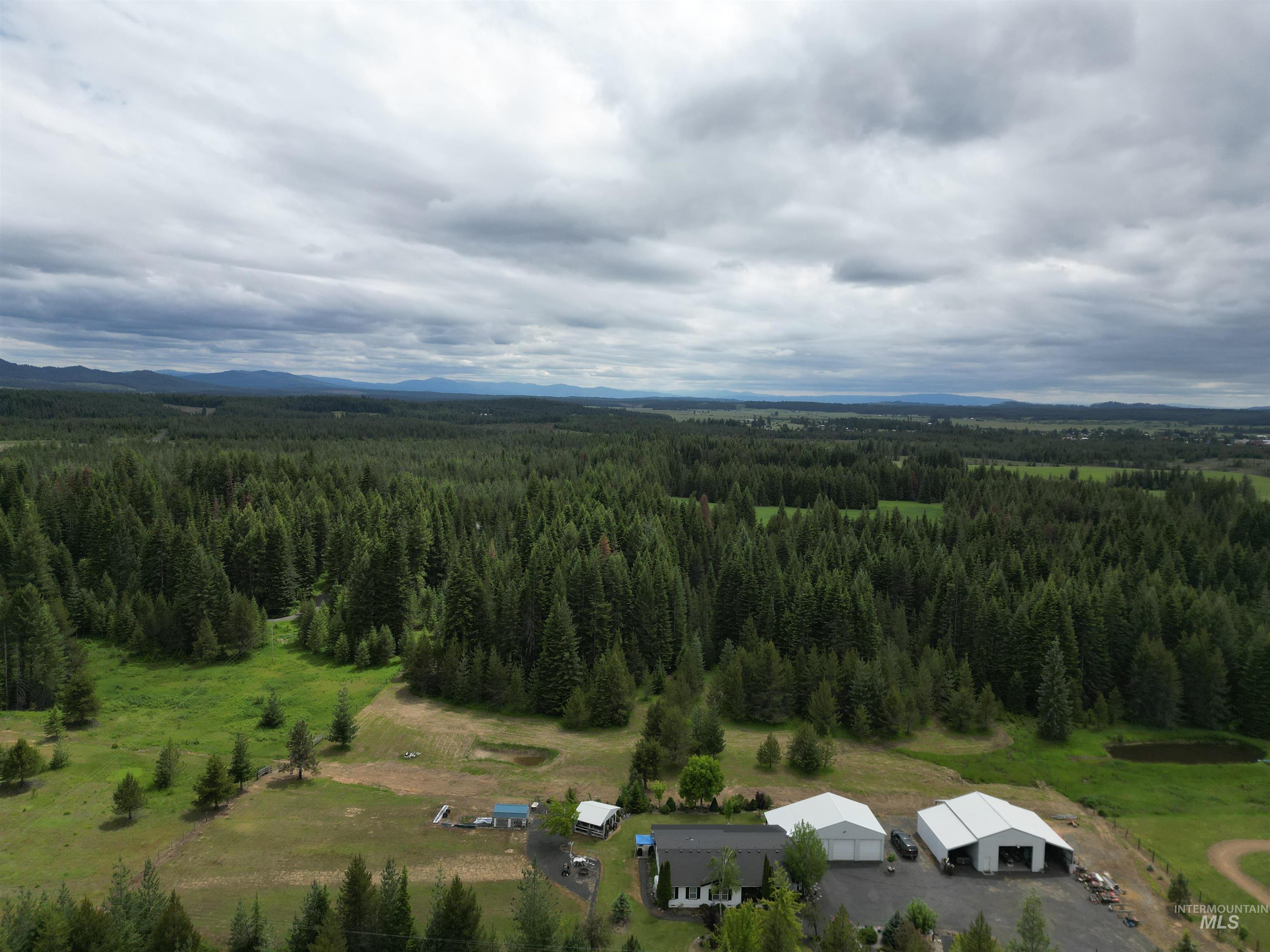254 Lackey Road Weippe, ID 83553 - Photo 35 of 38 Expansive property featuring a single-story residence, multiple large outbuildings, a circular driveway, and a pond, all surrounded by dense forest and open fields with distant mountains