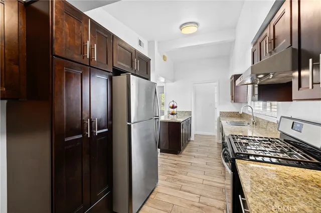 a kitchen with stainless steel appliances granite countertop a stove a sink dishwasher and a refrigerator with wooden cabinets