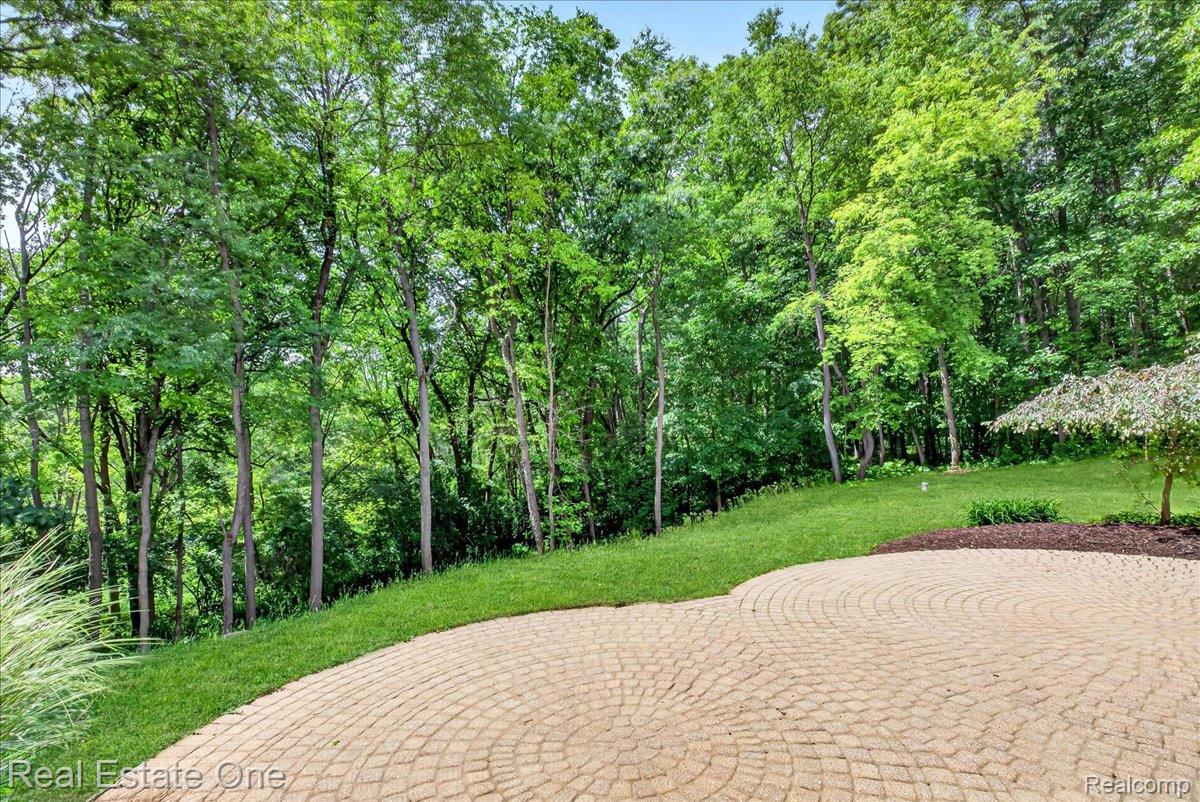 425 Courtney Road Leonard, MI 48367 - Photo 62 of 89 Expansive paver patio with a circular pattern, surrounded by a lush lawn and mature deciduous trees
