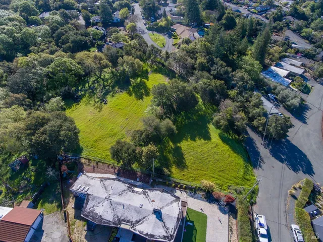 an aerial view of a residential houses with outdoor space and trees all around