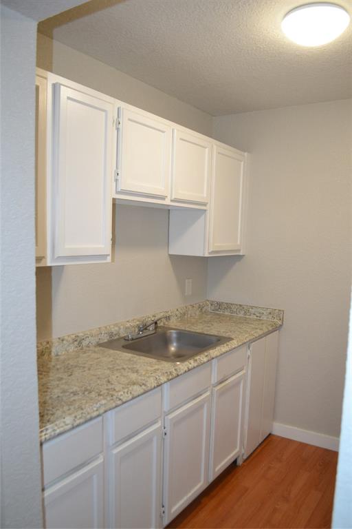 701 West Sycamore Street, Unit 207 Denton, TX 76201 - Photo 5 of 10 Kitchen with wood-type flooring, a textured ceiling, light stone counters, sink, and white cabinetry