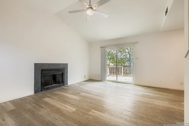 a view of an empty room with wooden floor fireplace and a window