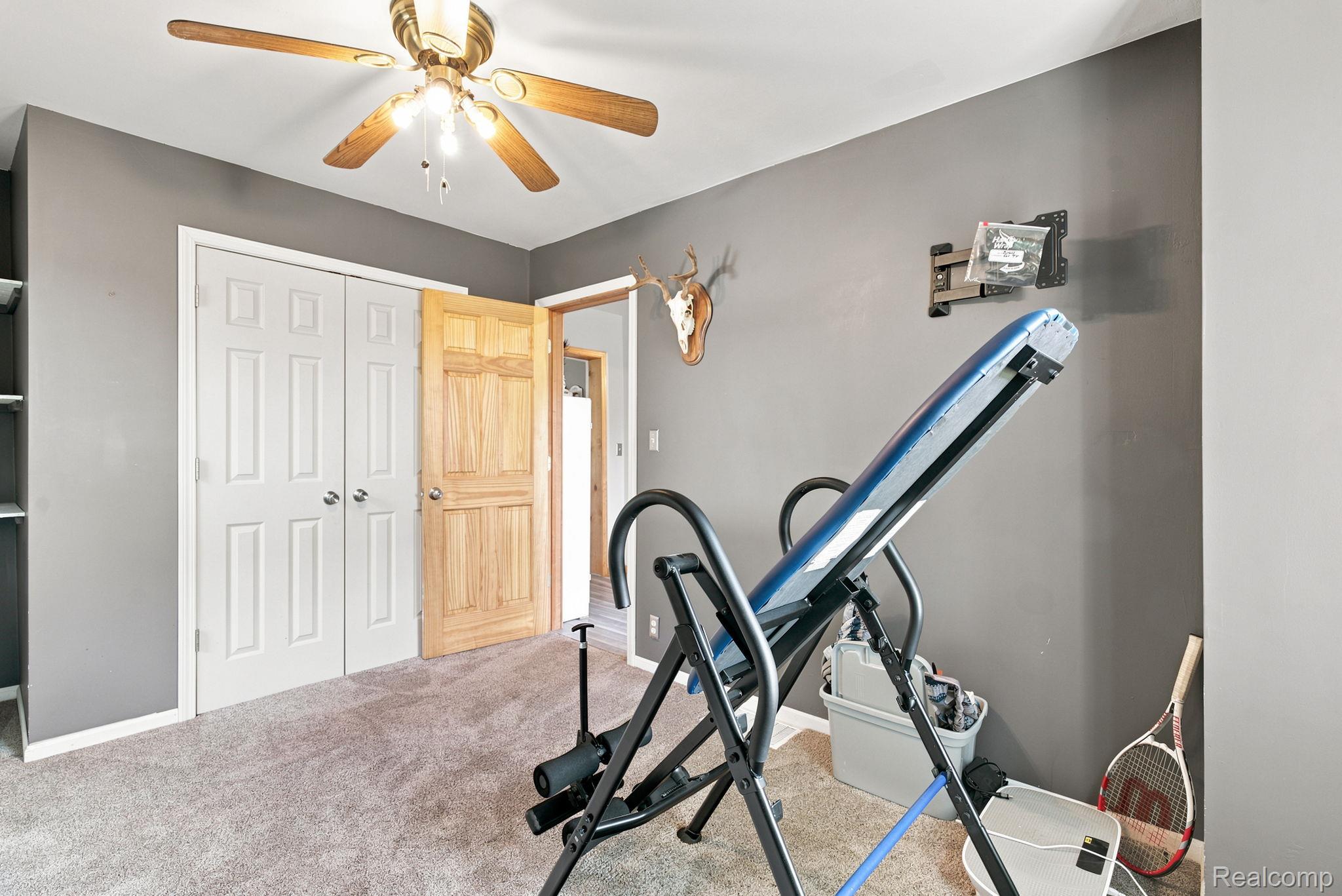 4201 Galbraith Line Road Croswell, MI 48422 - Photo 24 of 39 Carpeted room with gray walls featuring a ceiling fan with light fixture, built-in shelving, white bi-fold closet doors, and a natural wood door frame