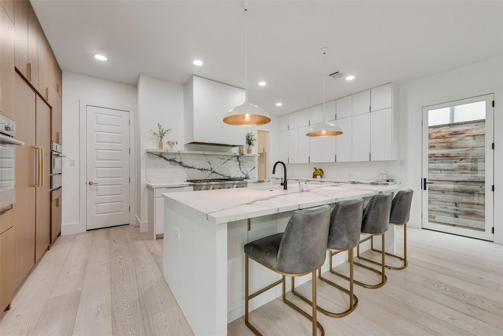 6443 Kenwood Avenue Dallas, TX 75214 - Photo 7 of 21 Kitchen with light wood finished floors, light stone countertops, a center island with sink, a kitchen bar, and hanging light fixtures